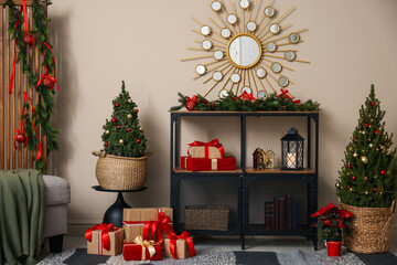 Shelving unit with Christmas decor between small spruce trees near beige wall indoors. Interior design