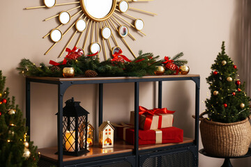 Shelving unit with Christmas decor and small spruce trees near beige wall indoors