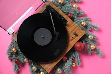 Obraz premium Wooden turntable with vinyl record and Christmas decor on pink background, flat lay