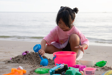 Happy Asian little girl playing with colorful sand toys on a tropical beach. Child digging sand with a blue shovel near the sea during summer vacation.