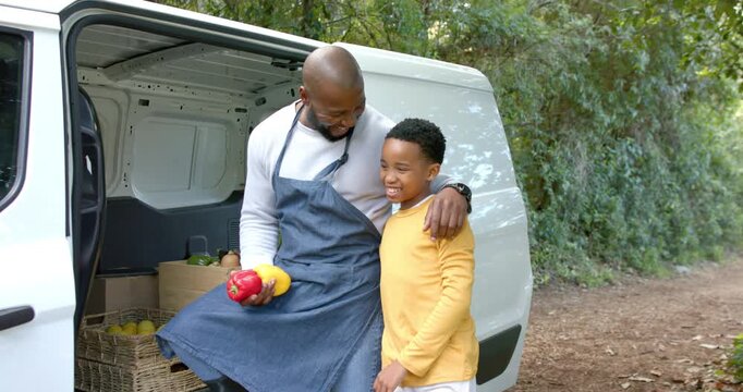Grabbing peppers African American father and son whispering laughing bonding at cargo van tailgate