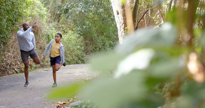 Walking trail, African American father and son warming leg muscles pointing at canopy, copy space - Powered by Adobe