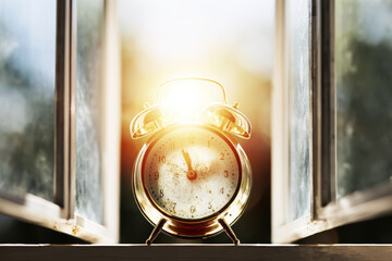Alarm clock morning sunrise on windowsill with sunlight glow and warm atmosphere