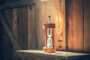 Antique hourglass sand timer wooden table sunbeam dust particles rustic barn vintage decor time concept