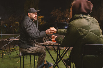 Friends share warm drinks at an outdoor cafe on a cool evening, enjoying casual conversation and connection under the night sky. Friendship, comfort, and urban life.