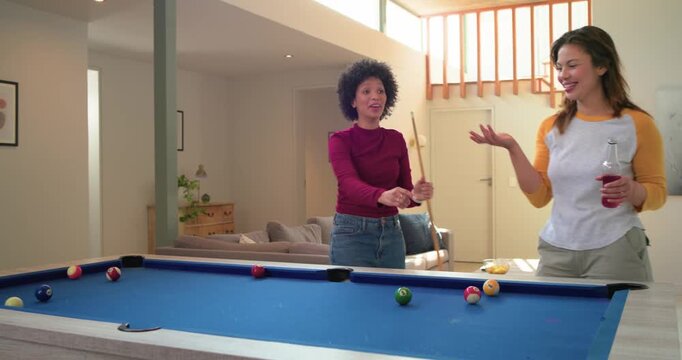 Missing shot sparking laughter while three female friends trading cues at home on pool table
