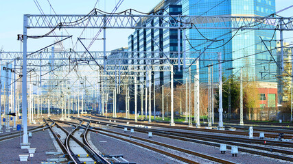 Tracks and electric high voltage for electric trains wires on reinforced concrete and metal masts against the backdrop of a city skyscrapers on a winter day.