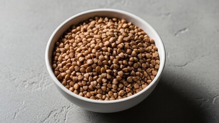 Full white bowl holds pile of brown buckwheat on gray surface in soft light