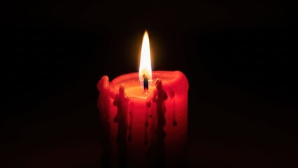 Glowing red candle flame on a dark background, wax dripping downward