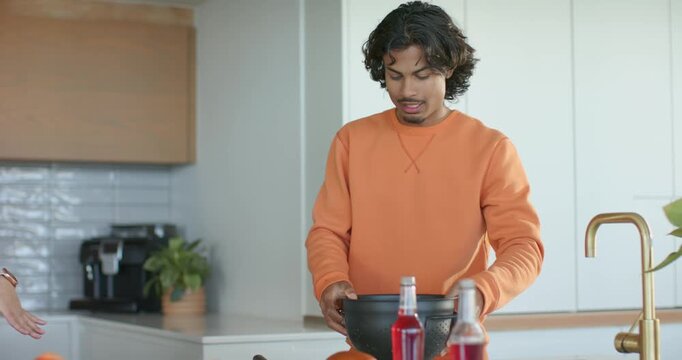 Diverse friends straining lettuce in colander layering on buns on counter after woman gesturing