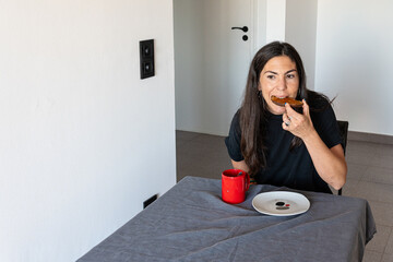 Woman having a meal, eating a slice of toast with a red mug on a gray tablecloth