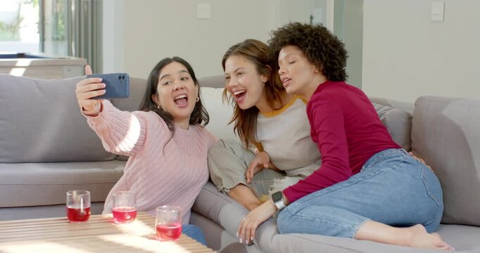 Three female friends lifting smartphone, capturing selfie and reviewing shot while laughing on sofa