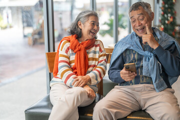 Senior asian couple using smartphone together sitting and smiling at cafe with digital technology, mobile banking, online shopping or telehealth services for elderly, modern lifestyle after retirement