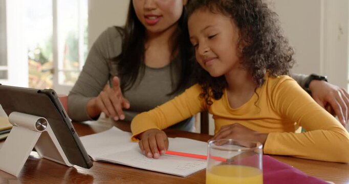 Mother and daughter after getting assignment pointing at tablet and writing in notebook at home
