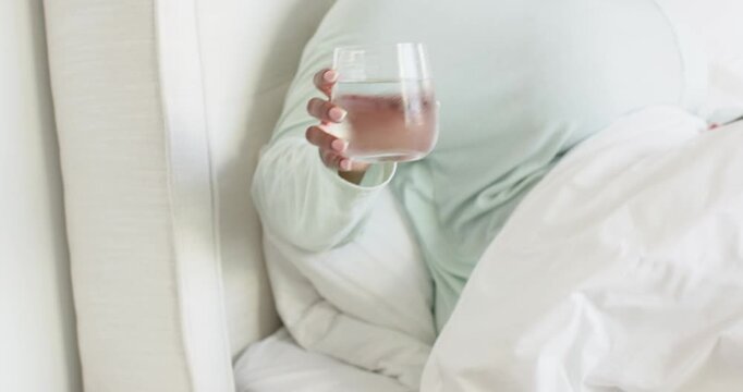African American mid adult woman grabbing glass on bedside table in bedroom, sipping water