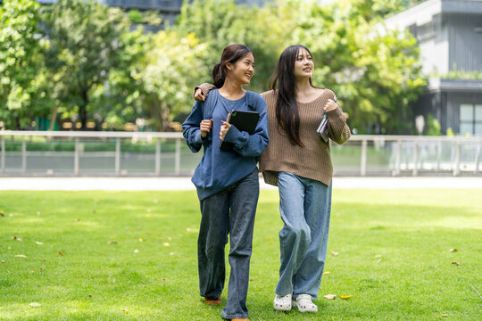 Two asian female students walk happy laughing and holding notebooks together at university, concept of education friendship student life, learning journey and joyful education, study and knowledge - Powered by Adobe