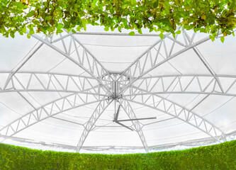 the structural steel framework that forms the main core of a modern dome-style fabric roof. It highlights both strength and contemporary design, surrounded by lush, vibrant greenery