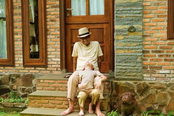 A father and son spending quality time sitting on the steps in front of a rustic brick house, enjoying a calm outdoor moment together.