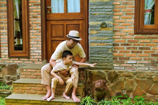 A father gently assisting his son as they walk down rustic stone steps outside a brick home, capturing a caring parenting moment.