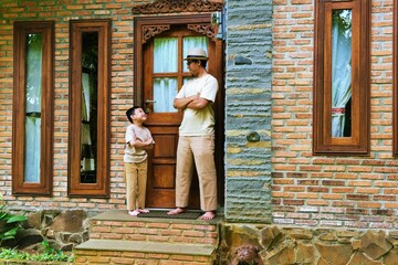 A father and son standing near the doorway of a rustic house, sharing a calm conversation during a peaceful outdoor moment.