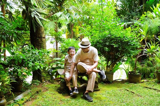 A father and his son sitting together in a green garden, enjoying calm bonding time surrounded by nature.