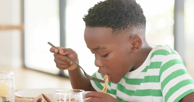 Hunger pushing African American boy spearing and slurping noodles at home dining table, copy space