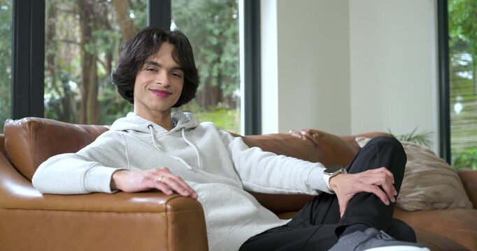 Man turning toward camera triggered by eye contact smiling while leaning on leather sofa by window