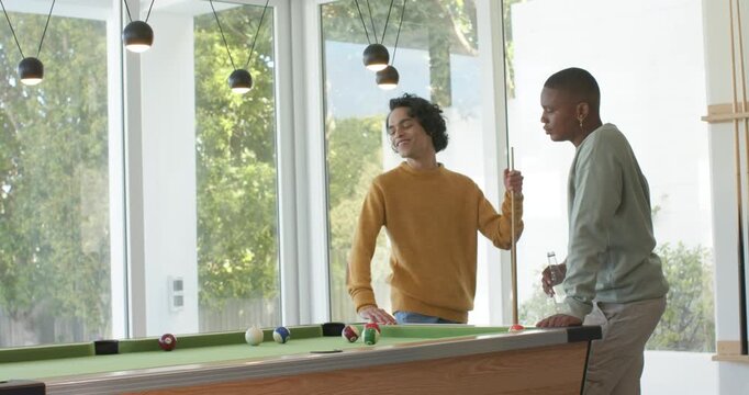 Diverse male friends aligning cues for strategic pool shot in rec room as new player entering