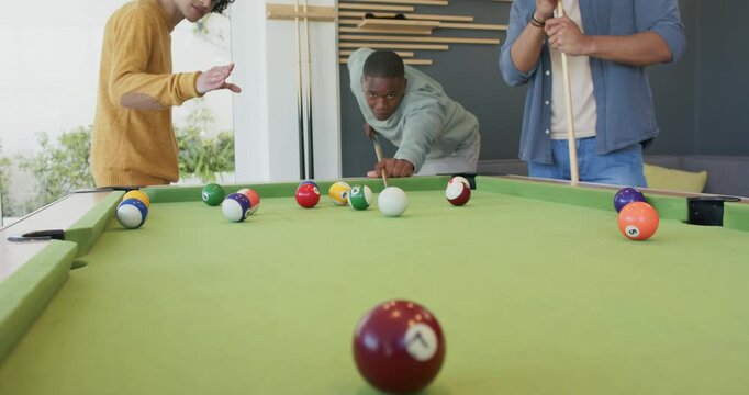 Encouraged by friend gesture, African American man taking shot at rec room pool table striking ball