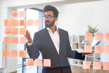 An Indian businessman uses sticky notes and a laptop to brainstorm ideas for a project