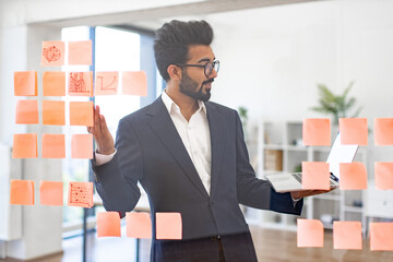 An Arabian businessman is working on a project with sticky notes and a laptop in a modern office setting