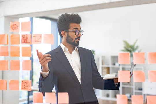 An Indian businessman in a suit uses sticky notes to brainstorm ideas in the office