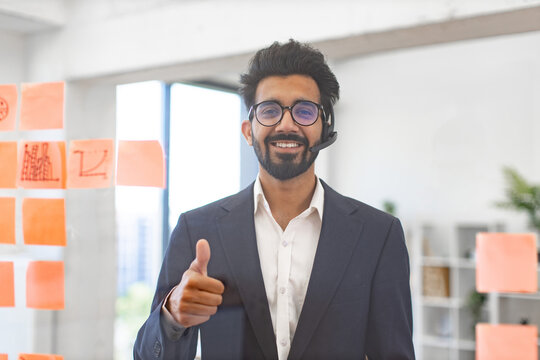 An Indian businessman wearing a headset gives a thumbs up, showing approval and support