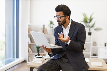 An Arabian businessman gestures while using a laptop during a video conference in his office