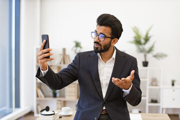 An Arab businessman in a suit gestures while on a video call using his smartphone