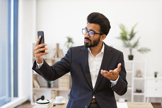 An Arab businessman in a suit gestures while on a video call using his smartphone