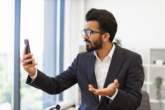 An Arab businessman in a suit looks frustrated while on a video call using his smartphone - Powered by Adobe