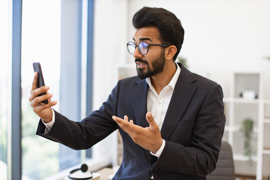 An Indian businessman in a suit gestures while on a video call using his smartphone - Powered by Adobe