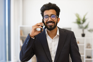 An Indian businessman smiles while talking on his cell phone in an office setting