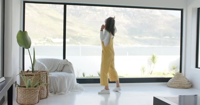 Hearing soft melody, woman is dancing in front of window with arm waves celebrating lake view