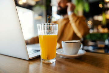 Close up of fresh orange juice on a table with smart casual freelancer working in a blurry background.