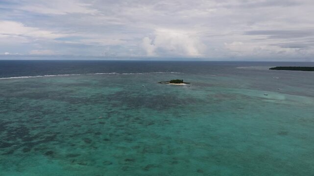 A small tree-covered island encircled by turquoise waters and coral reef patches under cloudy skies. Siargao, Philippines.