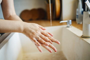 Person washing hands with soap and running water in sink