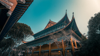 Naklejka premium Low angle view of a traditional chinese temple with green and orange roof tiles surrounded by trees under a blue sky