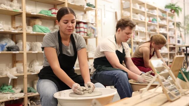 Female positive artisan in ceramics workshop with pottery wheel and various clay vessels. High quality 4k footage