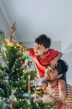 Father and child decorating Christmas tree together indoors