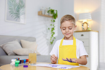 Cute little boy painting his handprint at wooden table indoors. Space for text