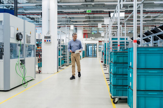 Engineer inspecting machinery with clipboard in modern production hall