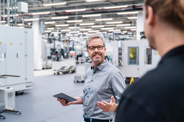 Engineer and employee having a meeting in production hall with machinery