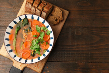 Tasty lentil soup in bowl and sliced bread on wooden table, flat lay. Space for text